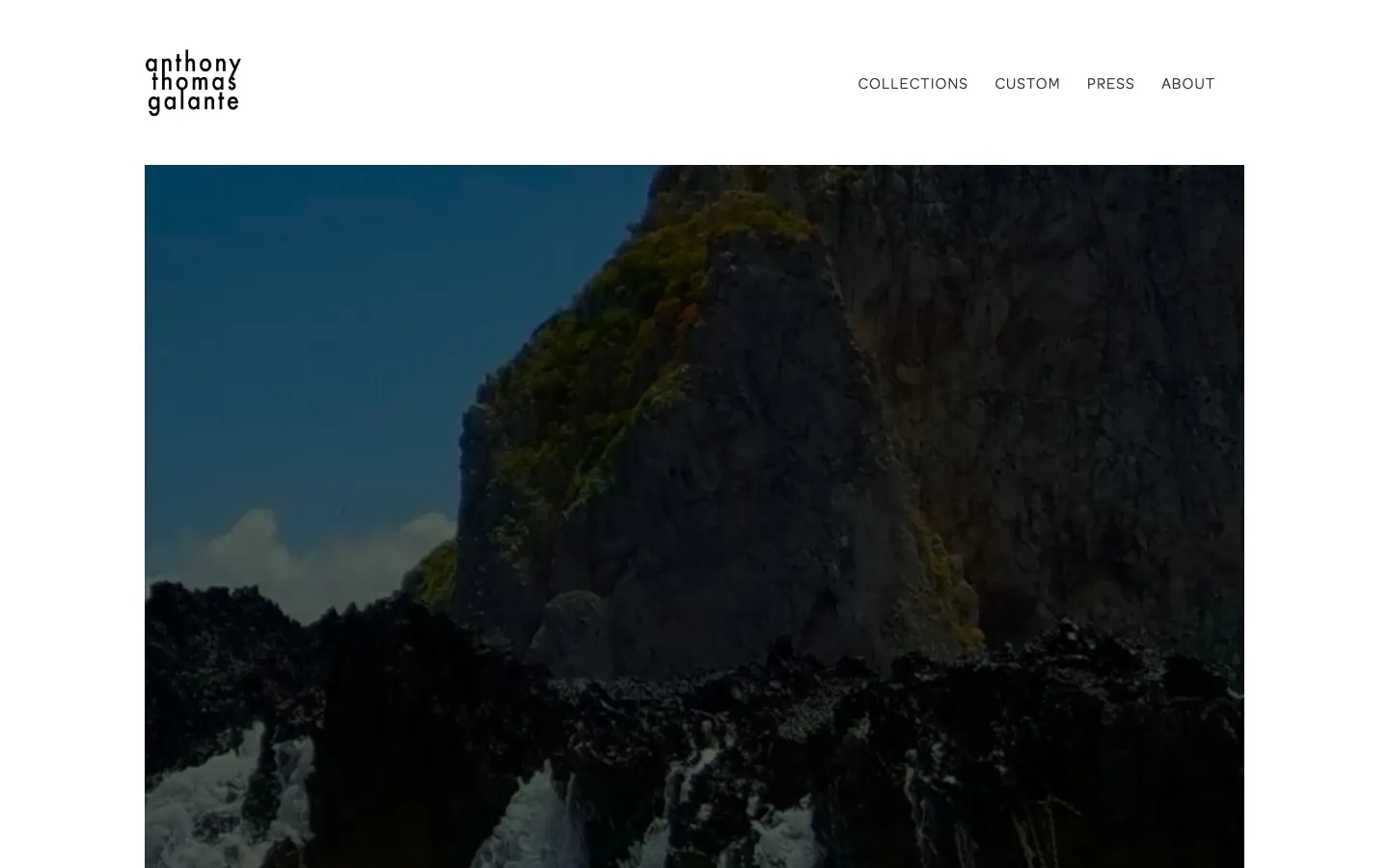 The anthonythomasgalante.com homepage: the lowercase "anthony thomas galante" wordmark with Collections, Custom, Press, and About navigation, above a full-bleed, moody photograph of a green-topped rocky sea cliff with waves breaking on dark rocks below.